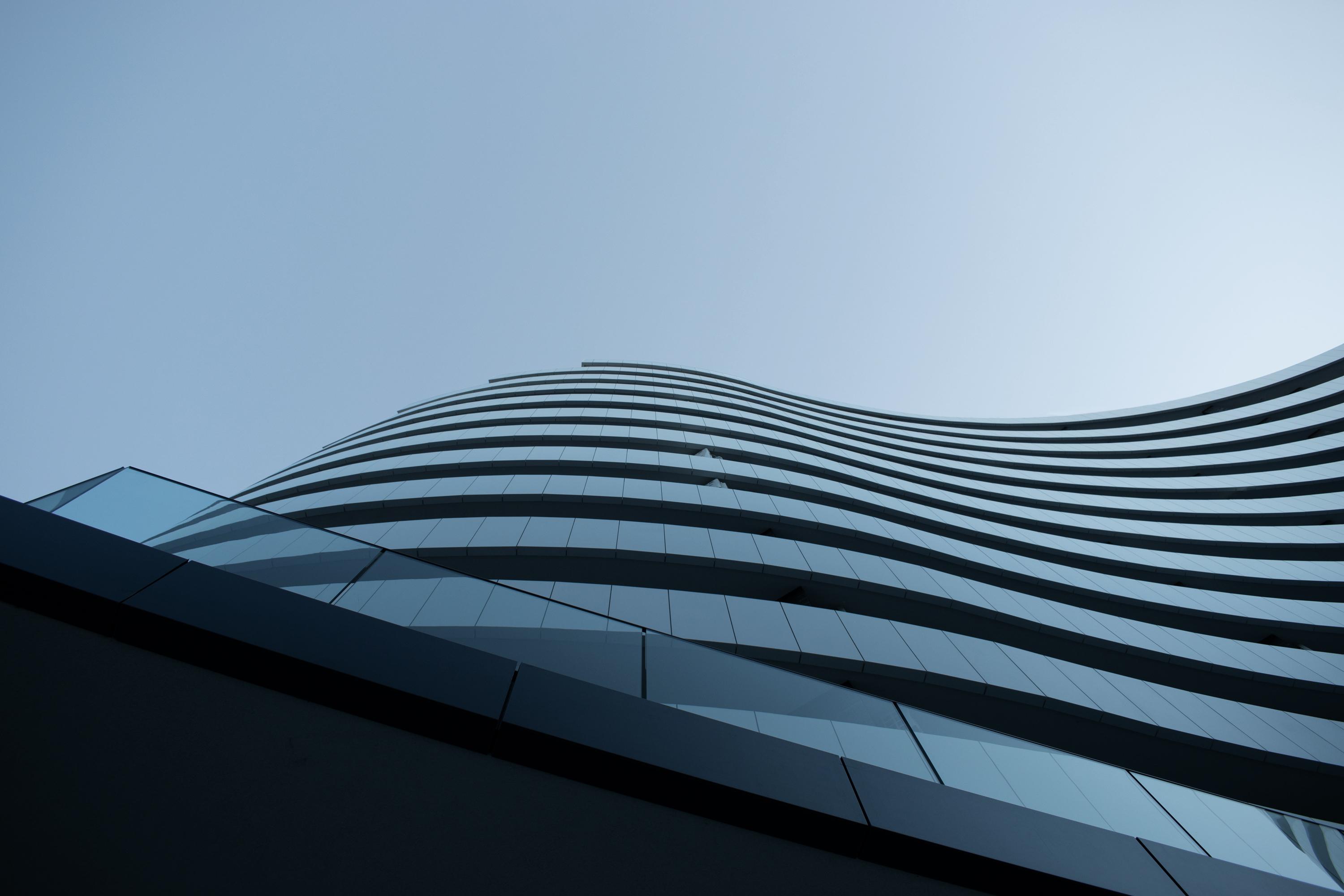 Close-up of an apartment building with glass panelled balconies and a blue sky background. 